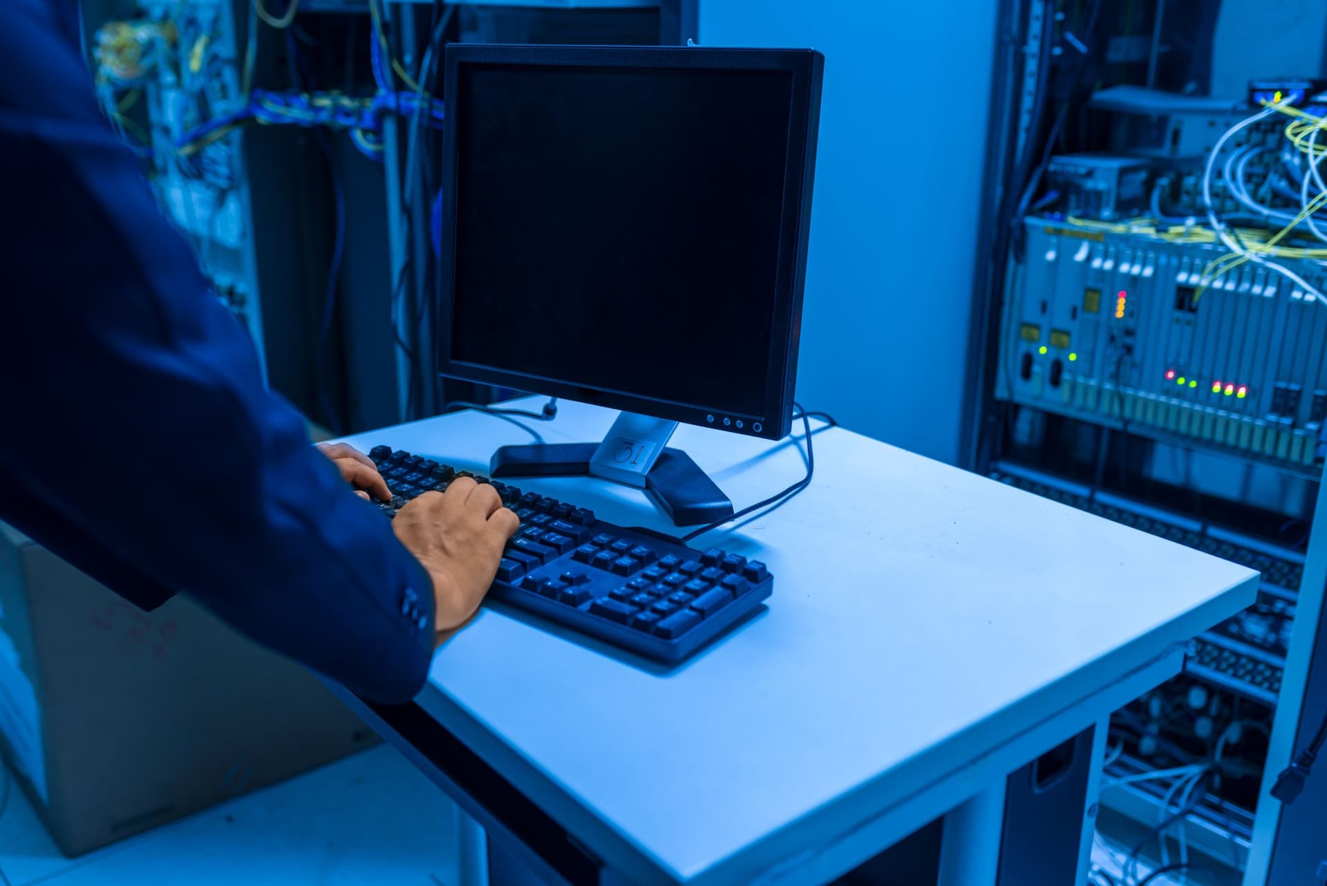 IT technician operating a workstation beside network equipment in a server room